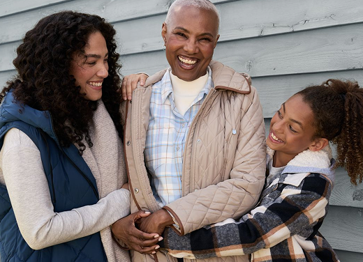 Three women smiling and hugging outdoors in winter clothing.