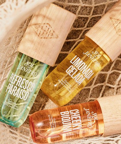 Three different scents of Sol De Janeiro perfumes laid out in netting over sand.