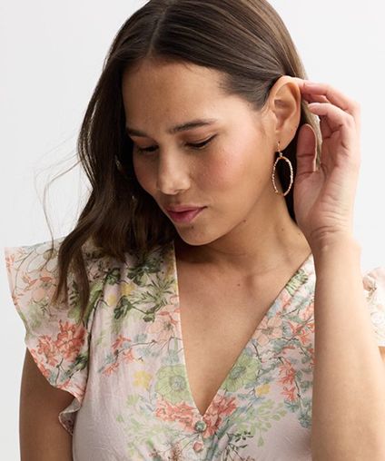 Woman in a floral dress brushing her hair back to reveal a hooped earring.