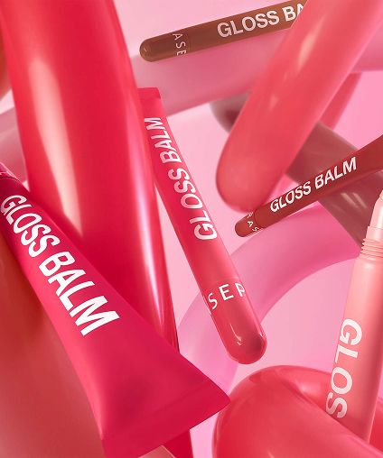 Different colored Gloss Balm containers mixed in amongst red and pink swirls.