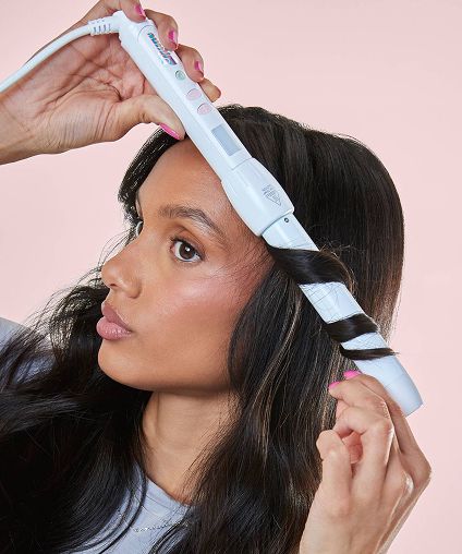 Woman styling hair with white curling wand.