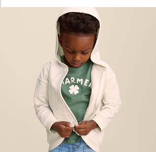 Child zipping up a hooded white sweatshirt with a green shirt underneath and jeans on.
