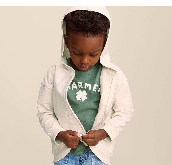 Child zipping up a hooded white sweatshirt with a green shirt underneath and jeans on.