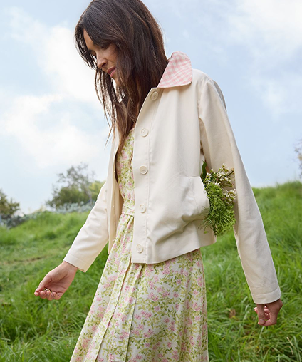 Woman in a field wearing a dress with a coat over it.