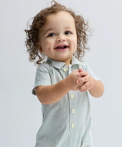 Small child smiling and clasping hands in a one-piece button up outfit - white with green stripes.