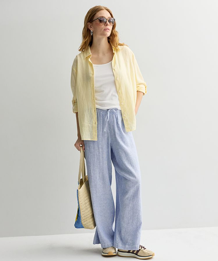 Woman holding a bag in a casual stance while wearing a linen overshirt and pants.