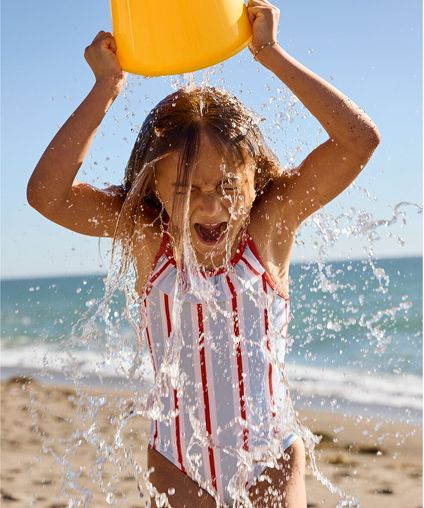 Young girl pouring water over herself at the beach.