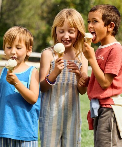 Three children eating ice cream cones outside.