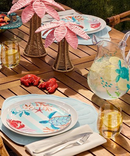 Outdoor dining setup on a deck table with mats, plates, silverware, and glasses.