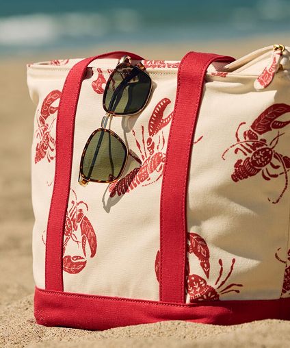 Beach bag on the sand in front of the waves with sunglasses draped over the bag edge.