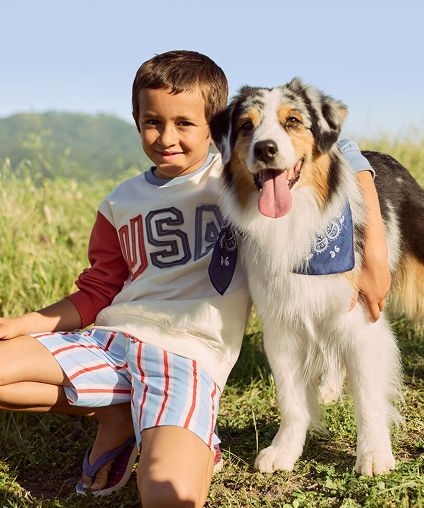 Small boy smiling outside with his arm around a dog.