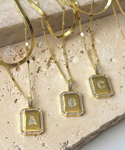 Three different initial necklaces lined up side by side.