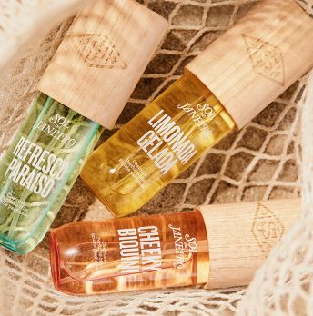 3 different bottles of SDJ fragrance mists in a net on beach sand.