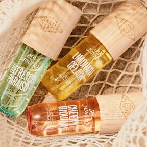 3 different bottles of SDJ fragrance mists in a net on beach sand.