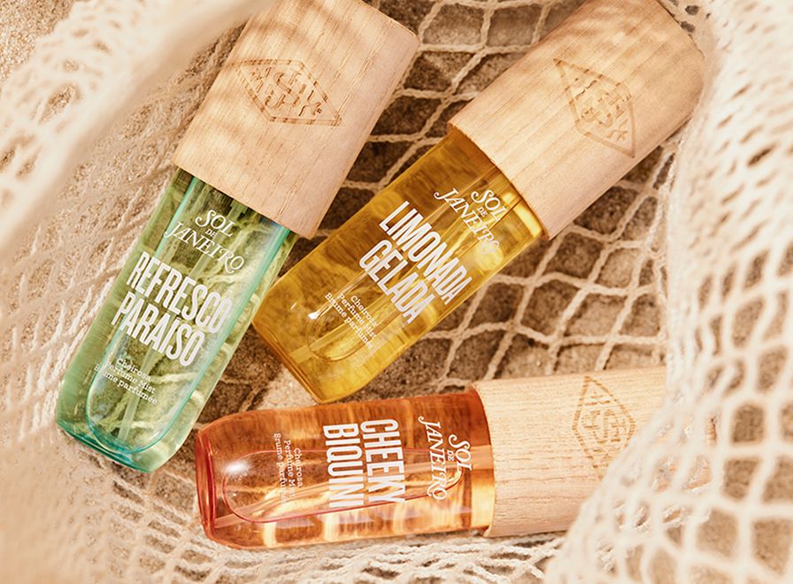 3 different bottles of SDJ fragrance mists in a net on beach sand.