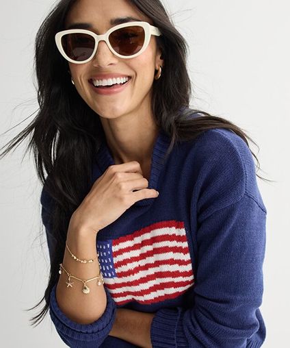 Woman with white sunglasses and a blue sweater with the United States flag on it.