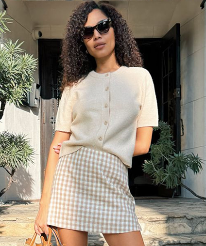 Woman wearing a beige button down shirt and checkered skirt with sunglasses.