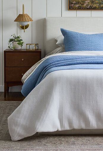 Bedroom with a night stand and a bed covered in a white blanket with a blue blanket folded on top.