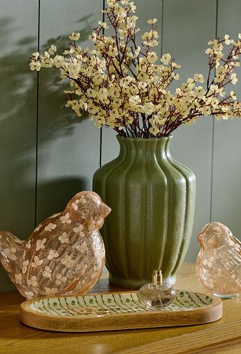 Various home decor items arranged in front of a green vase with yellow flowers.