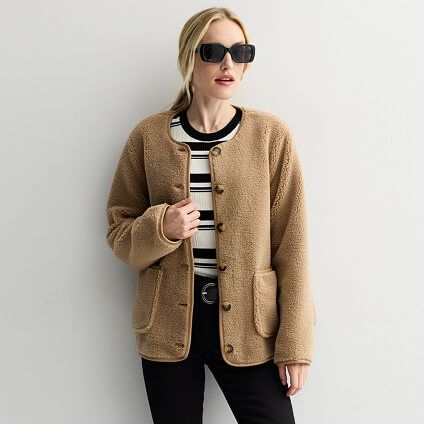 Model wearing a brown coat unbuttoned over a black and white striped shirt.