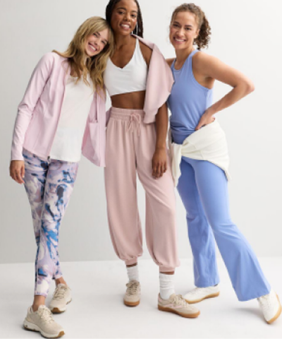 3 smiling women wearing various athletic gear embracing.