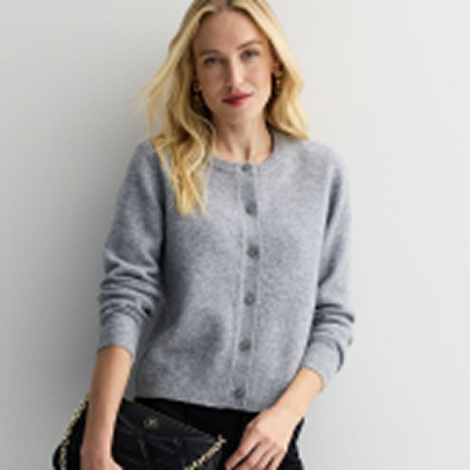 Model wearing a gray buttoned sweater and holding a black handbag.