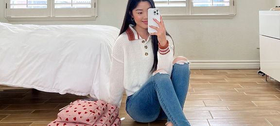 Woman wearing a white sweater and ripped jeans takes a mirror selfie