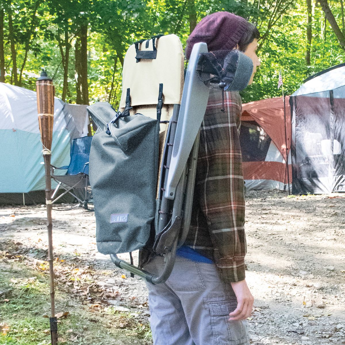 Person carrying gray two-tone folding camping chair with side storage.