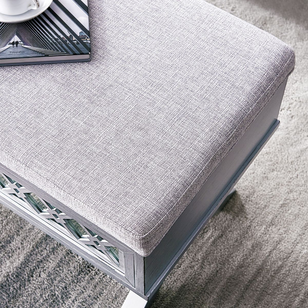Side view of light gray upholstered storage bench with diamond cutout front