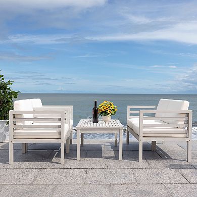 Two white cushioned outdoor chairs with a small wooden table facing the sea