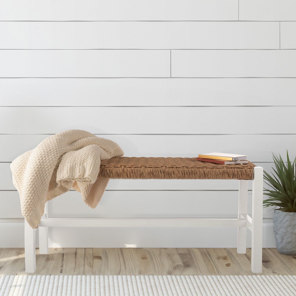 White entryway bench with woven rattan seat styled with throw and books