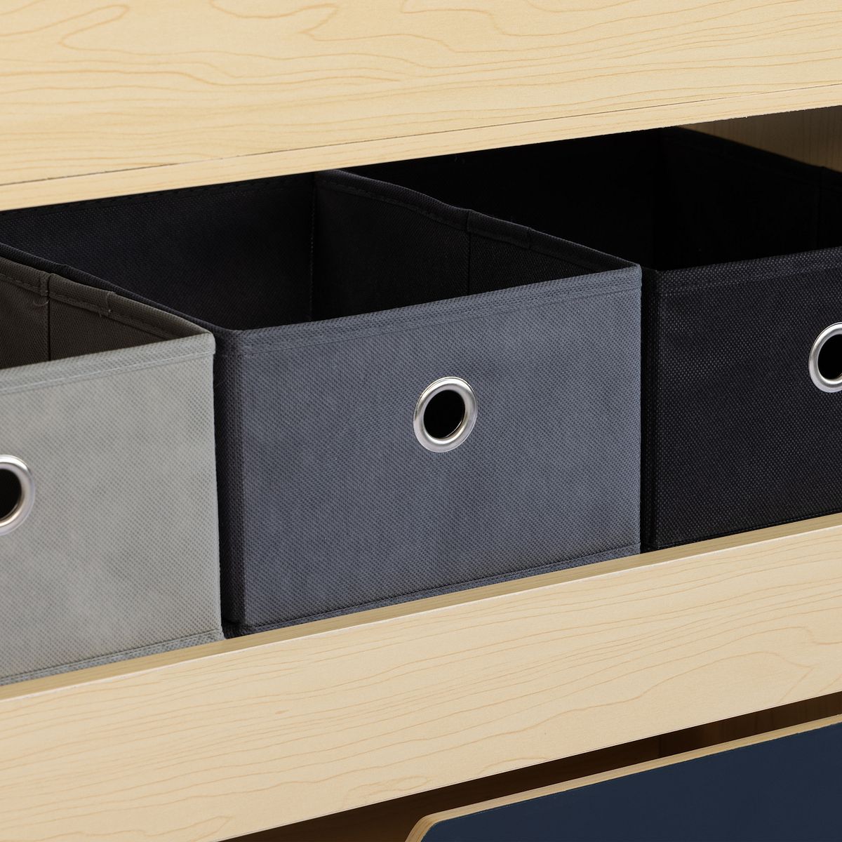 Close-up of fabric storage bins with circular grommet handles inside wooden cabinet