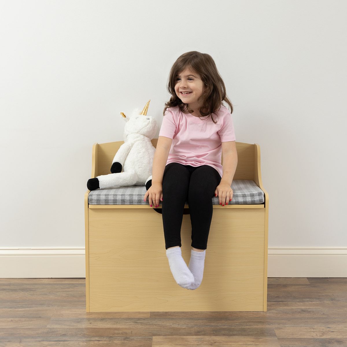Child sitting on Humble Crew hinged toy storage bench with plush