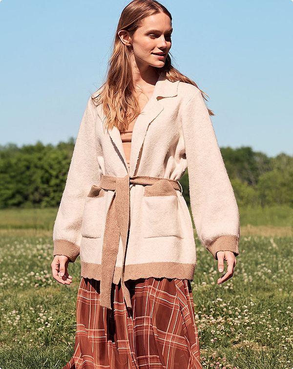 Androgynous woman in a field wearing oversized layered clothing 