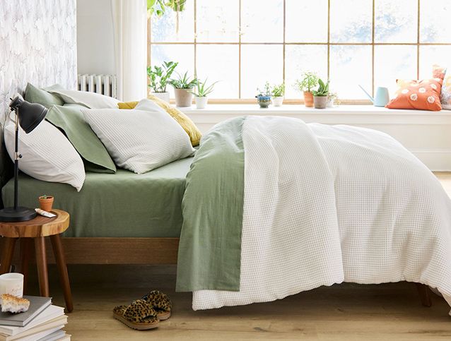 Bed with pillow and comforter set in front of large window with plants and decor